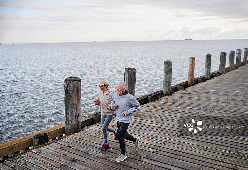 活跃的老年夫妇清晨在海边码头上慢跑图片素材