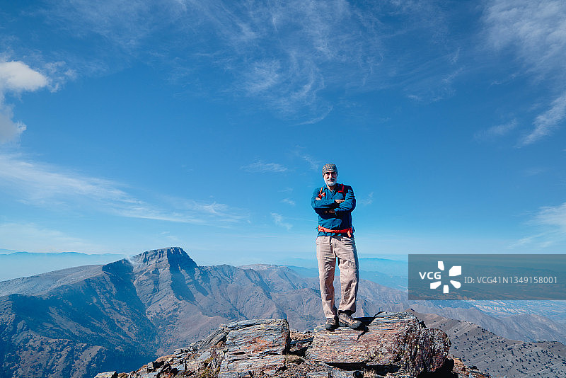 成功的年长登山者站在山顶，双臂交叉图片素材
