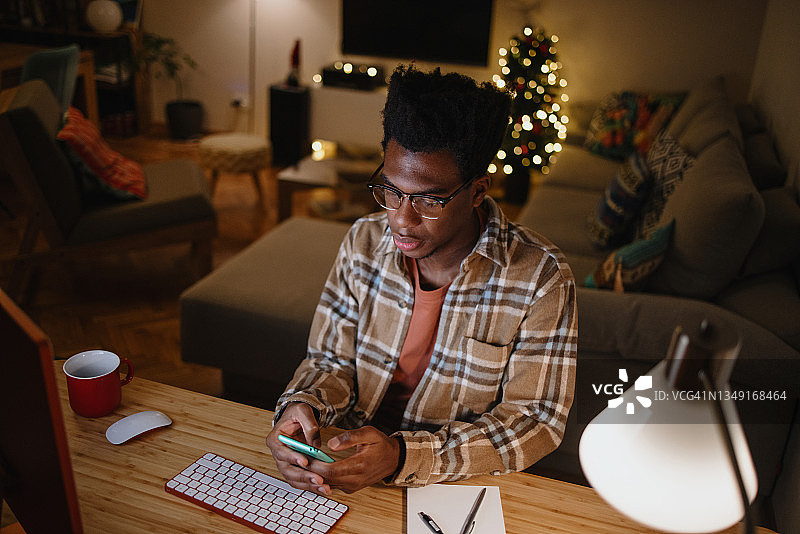 年轻男人在圣诞节期间一边工作一边发短信图片素材