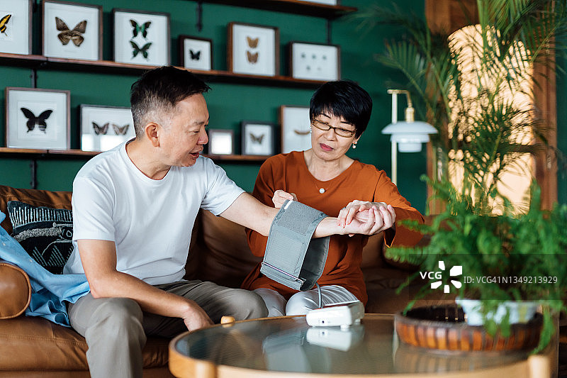 在家检查血压的年长的亚洲夫妇。妻子用血压监测仪检查丈夫手臂上的血压。老年人与保健概念图片素材