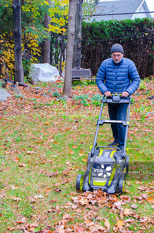 男子用割草机清理草地上秋叶图片素材