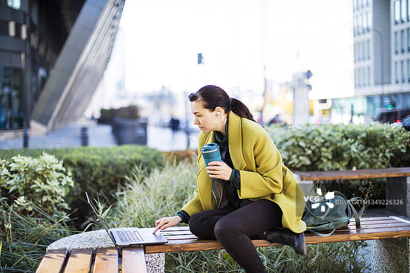 年轻女人在户外使用笔记本电脑喝咖啡图片素材