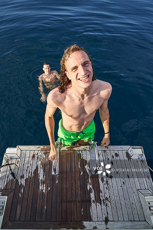 年轻的金发男子在海里游泳一段时间后，爬上船的楼梯图片素材