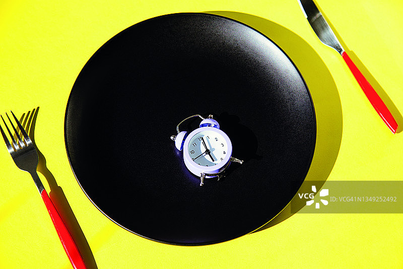 黄色背景餐具盘子上的闹钟图片素材
