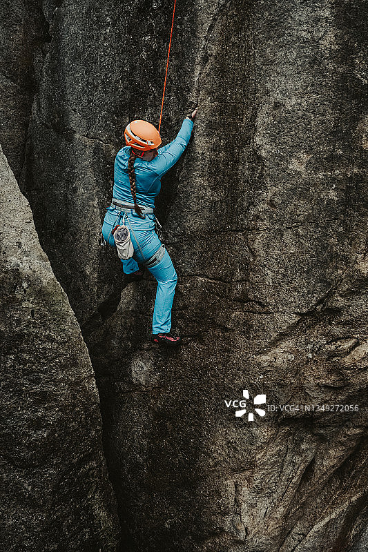 女性攀岩者在阴暗的一天穿着蓝色衣服攀岩图片素材