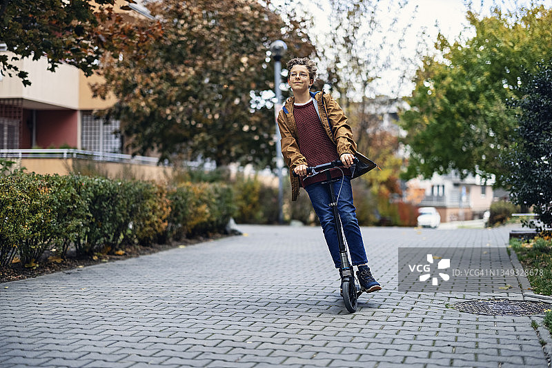 在住宅区骑滑板车的青少年男孩图片素材