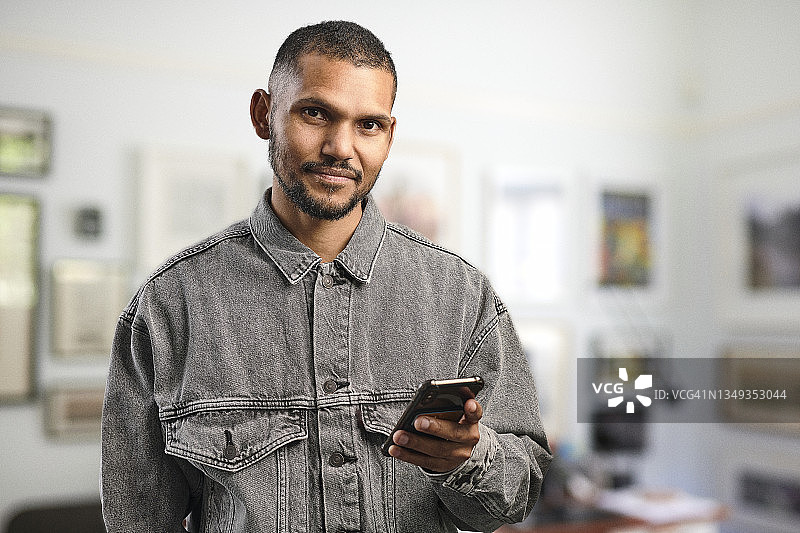 一位在家庭办公室手持手机的年轻男人肖像图片素材