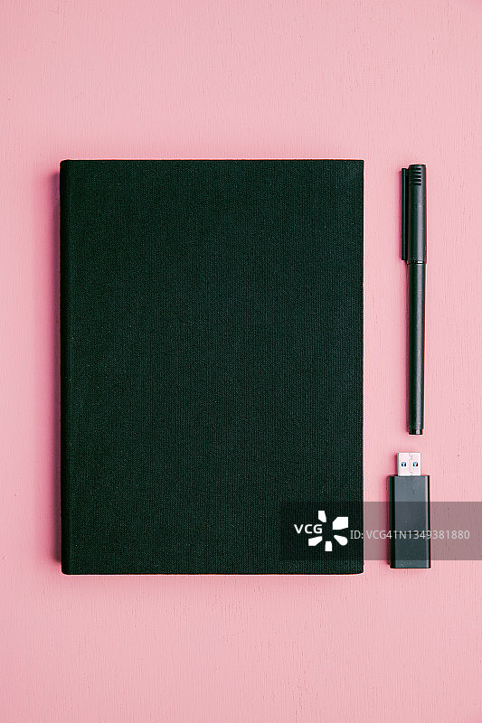 粉色桌子上的黑色笔记本、U盘和笔图片素材