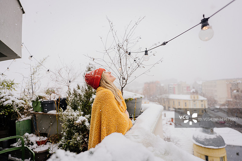 在寒冷的下雪天，裹着毯子在露台上的年轻女人图片素材