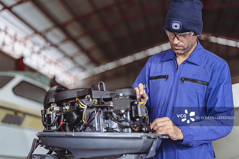 在车间修理舷外发动机的船舶机械师图片素材