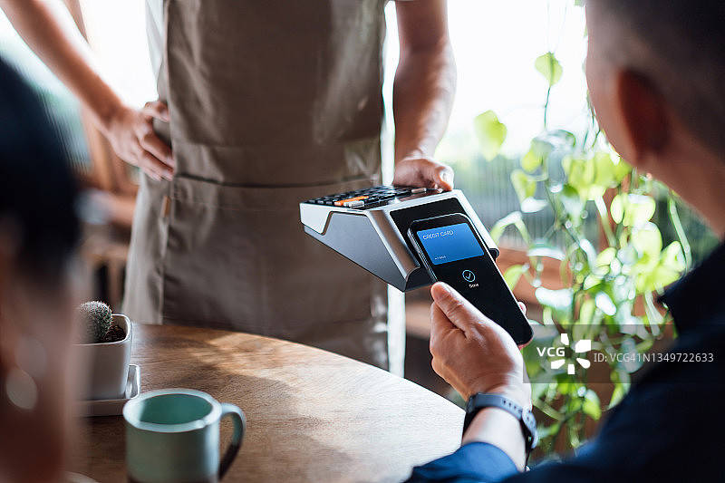年长的亚洲夫妇在餐厅用智能手机信用卡非接触式支付账单特写，在刷卡机上扫描。电子支付。老年人与科技图片素材