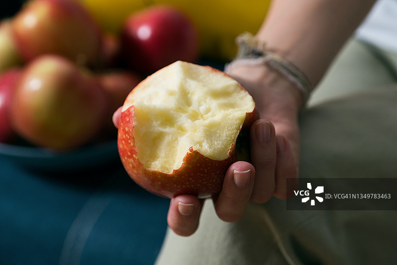 女子在家吃红色苹果，沙发色彩鲜艳。此图为素食、纯素食和健康饮食理念设计图片素材