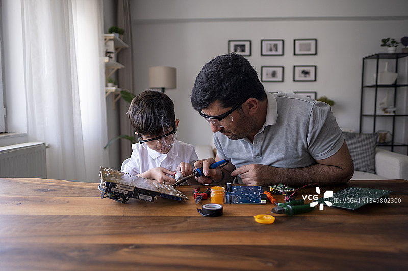 父子在家用电烙铁焊接电路板图片素材