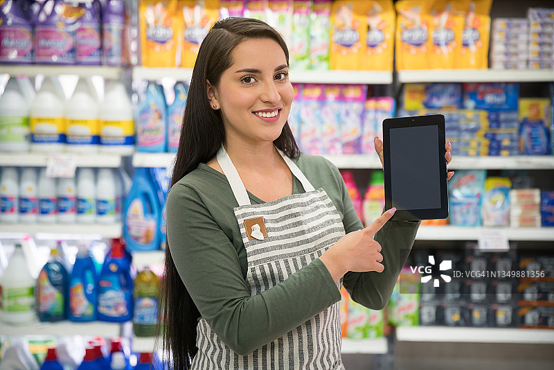 年轻漂亮的超市导购员拿着平板电脑，展示屏幕图片素材