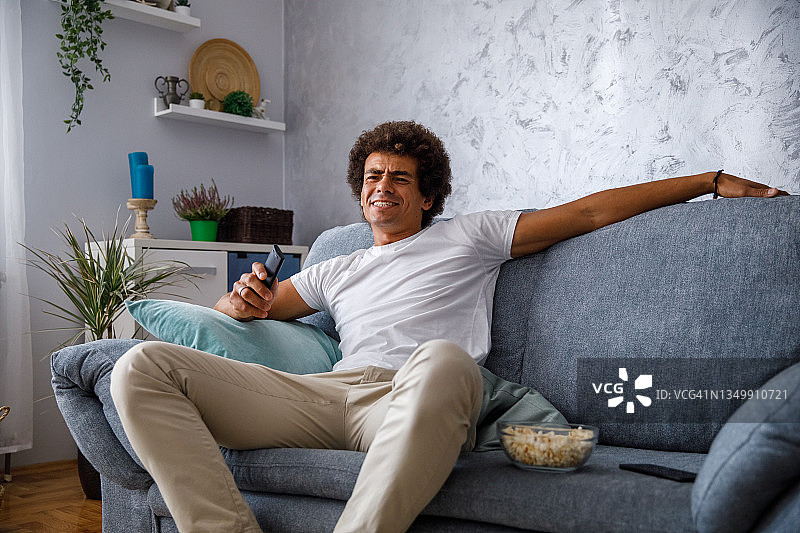 年轻男人躺在沙发上看电视，并做着鬼脸图片素材