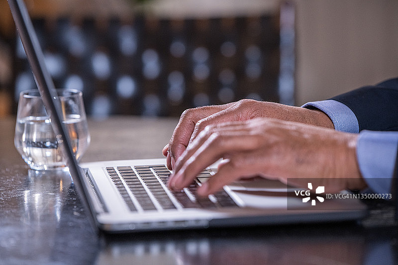 阳光明媚的办公室里，深色皮肤的男人在笔记本电脑键盘上打字，商业和科技概念。特写。在家工作。图片素材