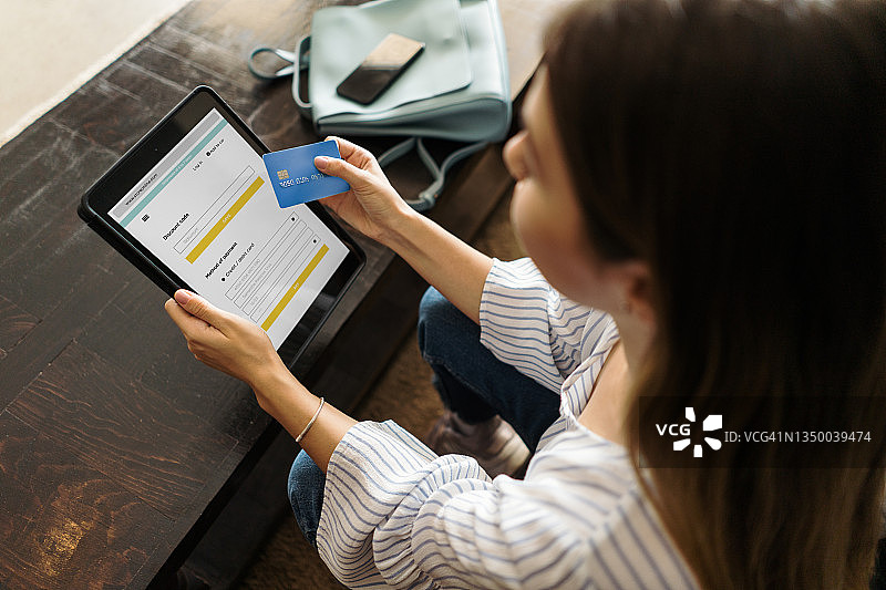 女人手持蓝色信用卡，使用平板电脑进行在线购物图片素材