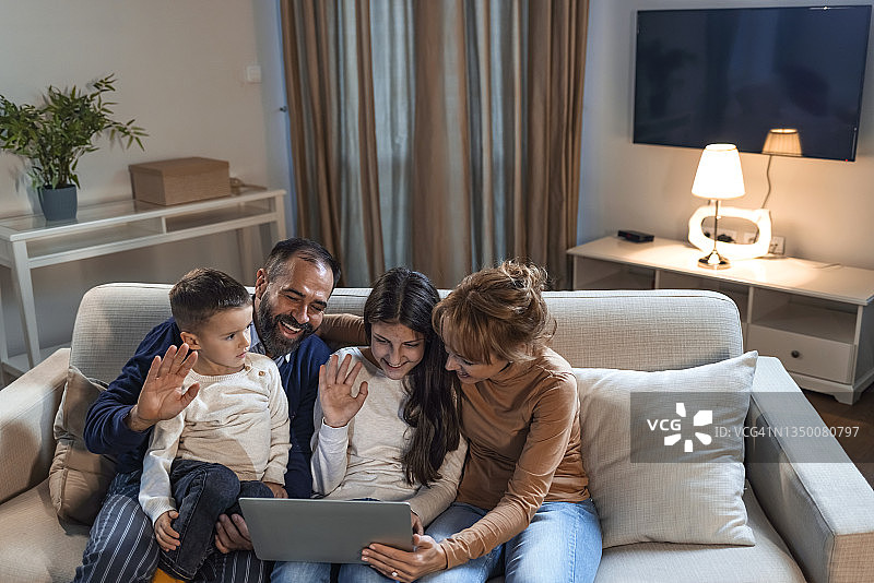快乐的父母和孩子们在沙发上笑着使用设备图片素材