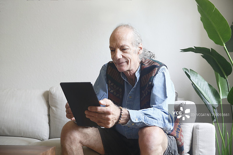 坐在客厅沙发上，使用平板电脑的年长的白人男子图片素材