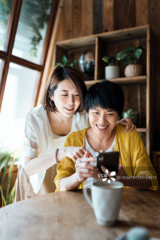 亚裔老母亲和女儿在家一起使用智能手机，快乐地微笑，享受母女亲情时光。多代同堂家庭和科技图片素材