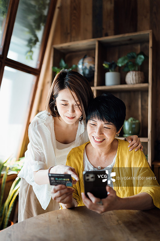 快乐的亚洲母女在家用智能手机网购，并用信用卡付款图片素材
