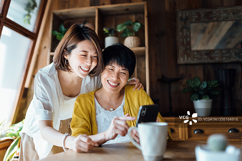 亚裔老母亲和女儿在家一起使用智能手机，快乐地微笑，享受母女亲情时光。多代同堂家庭和科技图片素材