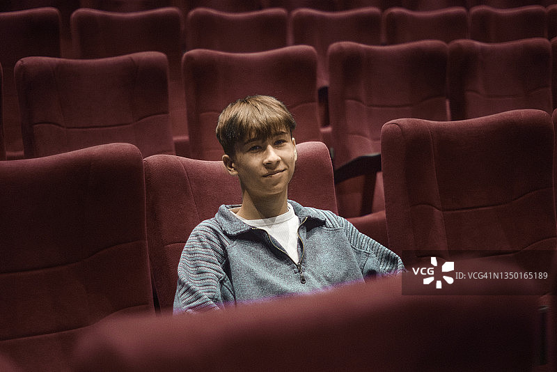 坐在电影院红色座椅上看向镜头的快乐少年肖像图片素材