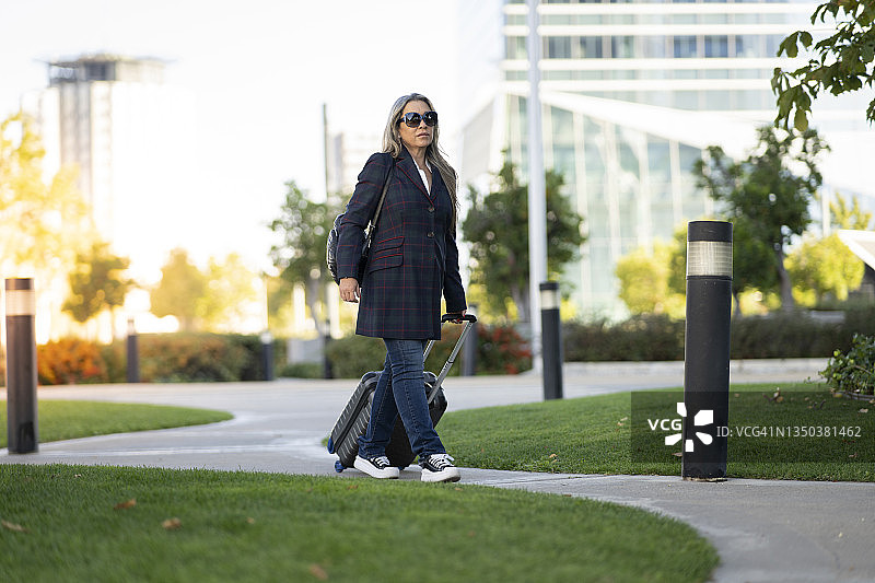 在城市里，一位带着行李箱和太阳镜的中年妇女图片素材