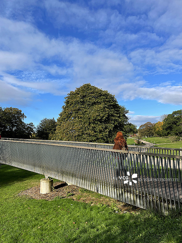 长发红衣女子在秋日阳光下行走，背着背包走过木桥图片素材