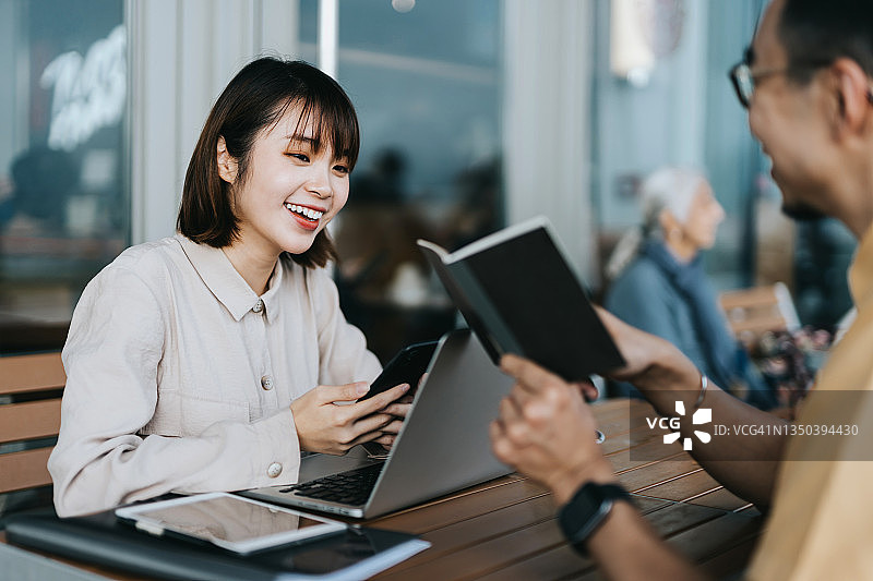 在咖啡馆户外讨论业务并在笔记本电脑上一起工作的年轻亚洲同事图片素材