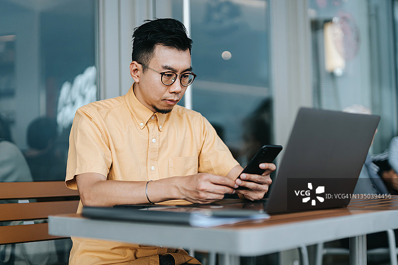 在咖啡馆户外使用智能手机和笔记本电脑的自信亚洲年轻商人，随时随地办公概念图片素材