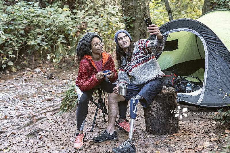 情侣在树林露营帐篷旁用手机开心地自拍图片素材