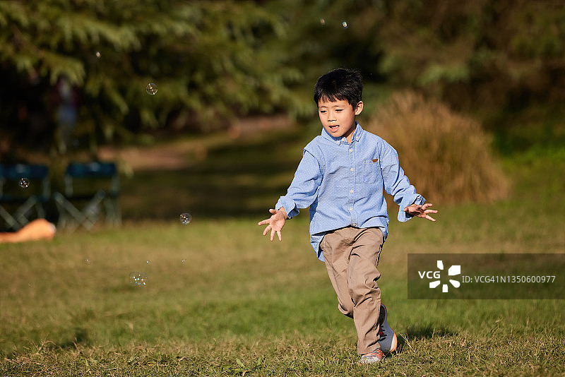 亚洲男孩在公园里快乐地追逐泡泡图片素材