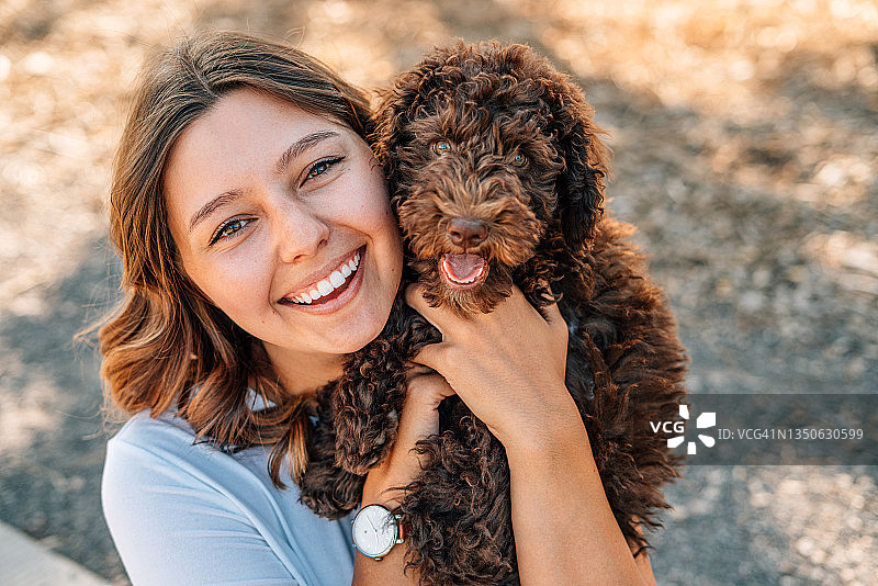 快乐的年轻女子抱着可爱的“绵羊杜德尔犬”蓬松狗的特写肖像图片素材