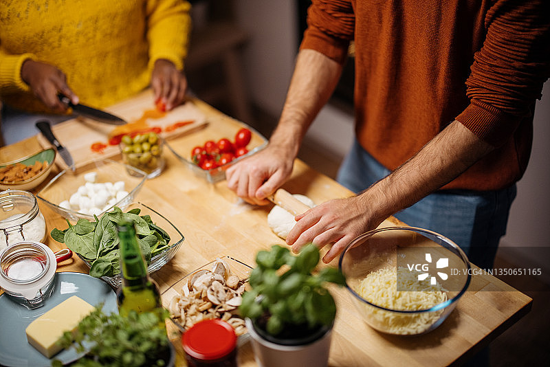 年轻男人用擀面杖擀面，年轻女人正在切披萨的配料图片素材