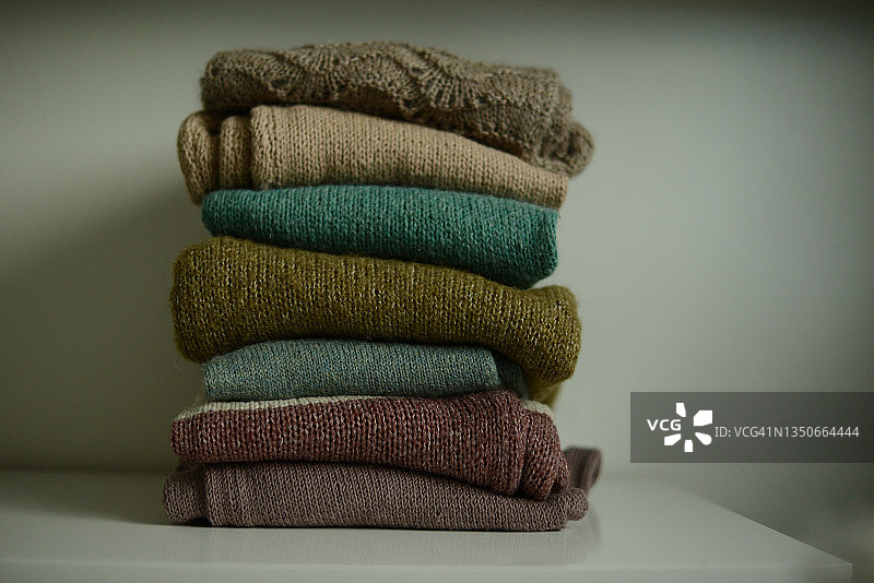 白色架子上棕色和绿色色调的一堆针织毛衣图片素材