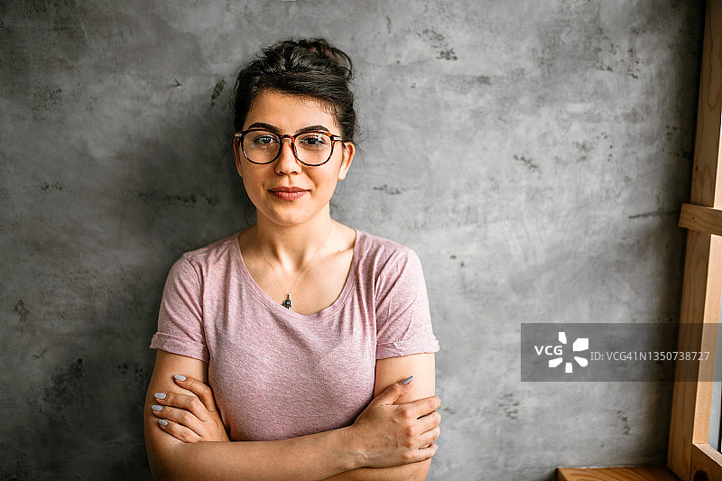 在现代办公室靠着灰色混凝土墙的年轻女企业家图片素材