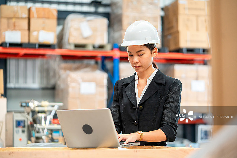 年轻有魅力的亚洲女员工或实习生在仓库商店通过电脑进行库存盘点。亚洲店主或小企业概念图片素材
