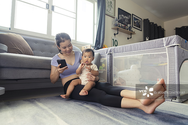 年轻的亚洲妈妈在家锻炼后，用手机和信用卡与女儿一起在线购买婴儿玩具图片素材
