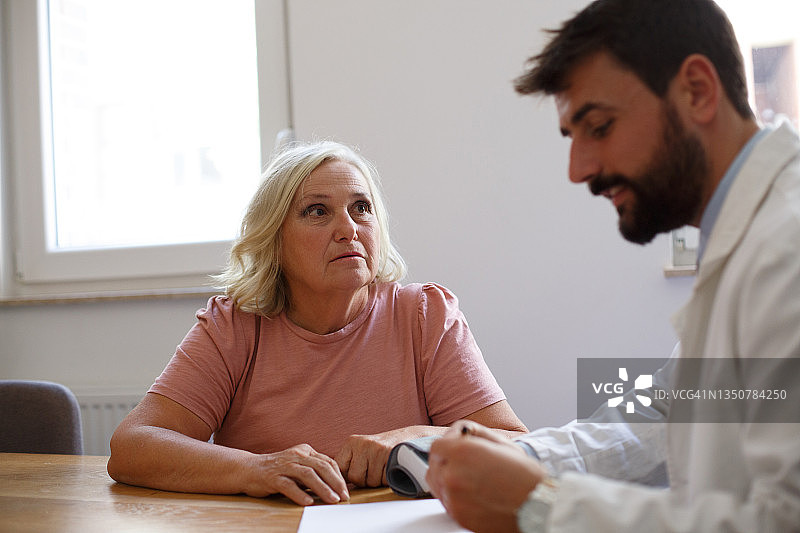 年长的女士在医生处就诊，年轻医生正在提供建议。图片素材