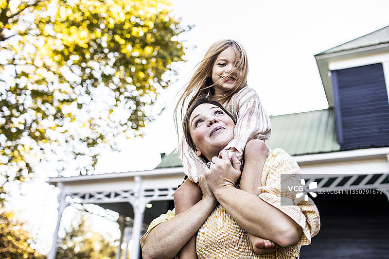 母亲在农舍前肩上扛着女儿图片素材