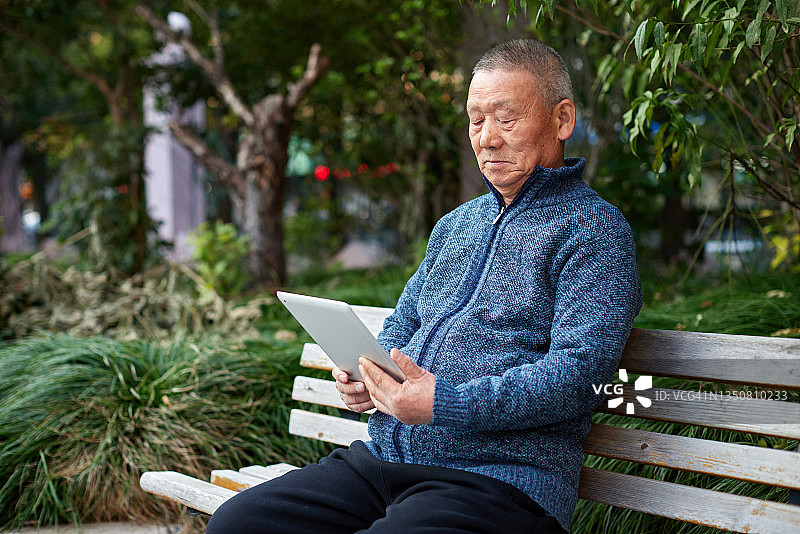 坐在长凳上使用平板电脑的亚洲老年男性图片素材