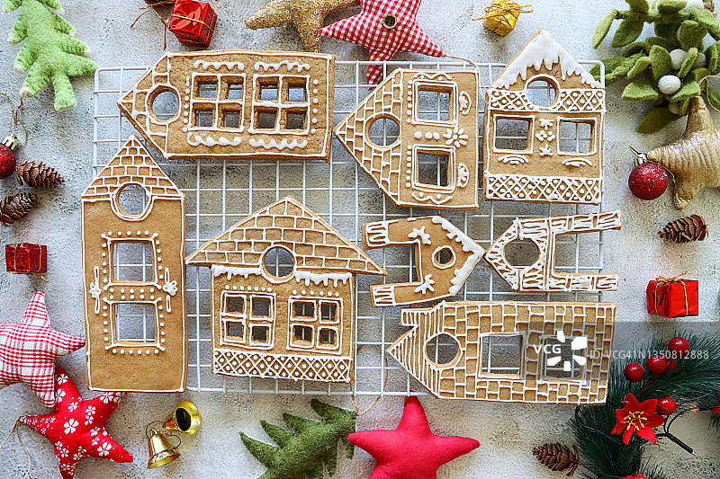 自制房屋形状姜饼饼干图片，饼干上涂有白色糖霜，位于白色金属冷却架上，圣诞村展示周围环绕着毛毡圣诞树和星形装饰品，大理石效果背景，高角度视图图片素材