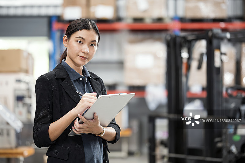 仓库管理系统中库存水平追踪：女仓储工人手持库存清单，处理仓库中每个物品的库存状态，以满足客户订单图片素材