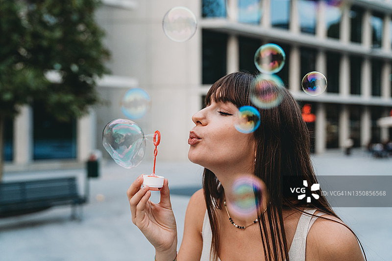 在日落时分的城市里玩泡泡棒的年轻女子图片素材