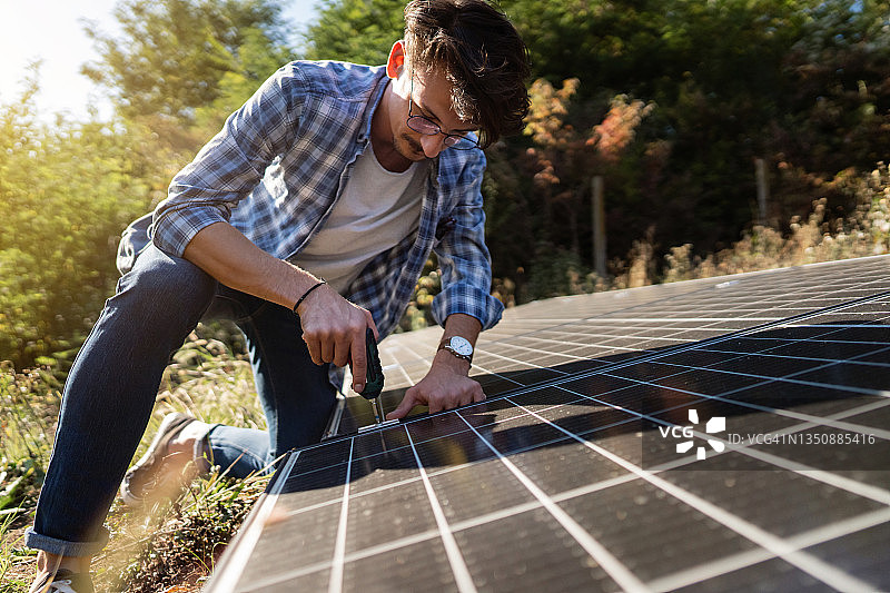 用钻头在院子里安装太阳能电池板的白人男子图片素材