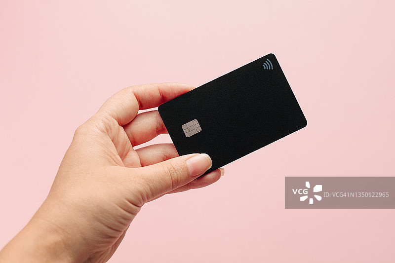 女性手持黑色银行卡在粉色背景前图片素材