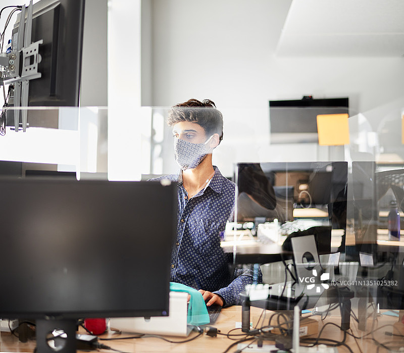 戴着口罩在屏幕后办公桌工作的年轻商人图片素材