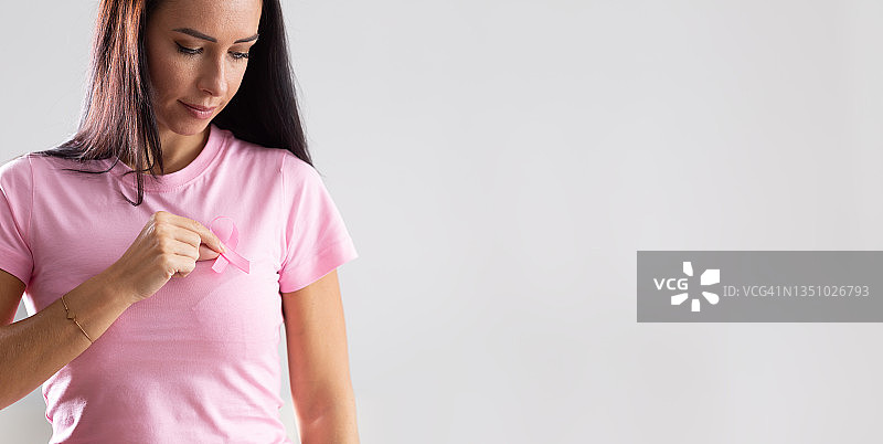 在隔离背景下，穿着粉色T恤的女人胸前拿着粉色丝带，象征着预防乳腺癌图片素材