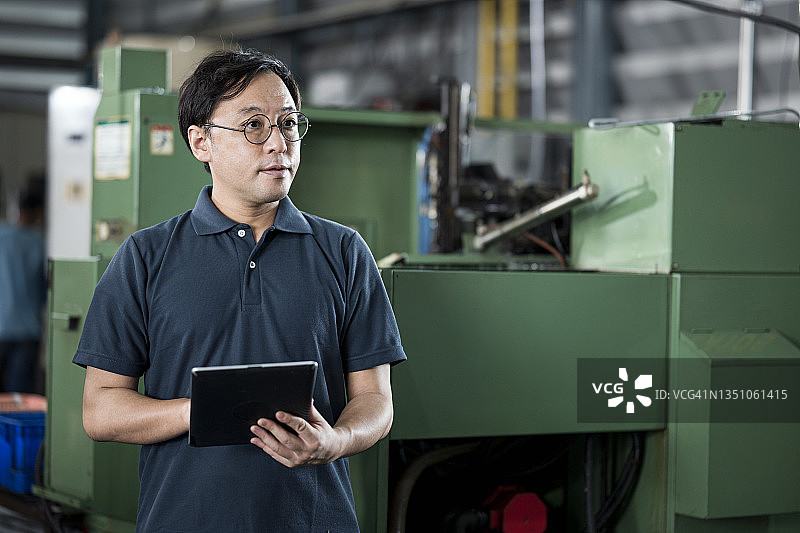 制造业改进估值和成本核算能力。工厂主在数控铣床上使用平板电脑，在工程零件生产线上工作。图片素材